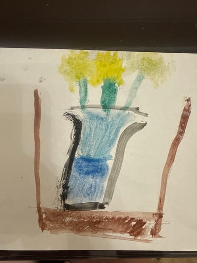 The image shows a child's watercolor painting on off-white paper. The painting depicts an abstract scene with a prominent blue and gray form in the center, possibly representing a building or a large object. To the left of this central form, there are splotches of yellow and green paint, suggesting trees or foliage. A brown, rectangular frame encloses the right side of the painting, with a horizontal brown line running across the bottom. The painting has a primitive, expressive style characteristic of young children's artwork. No people are visible, and the scene is abstract. There are no discernible details indicating time of day, weather, specific location cues, or emotions. No text is visible in the painting. The background of the original image shows a dark, textured surface on the left and a dark frame on the right, suggesting the painting is matted or framed. The context of Vinnytsia, Ukraine, does not provide any specific visual cues within the artwork itself.