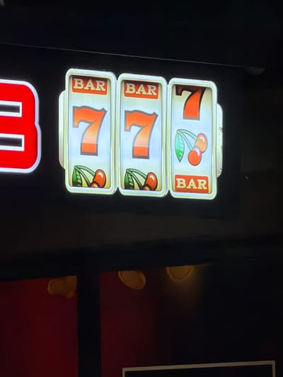 The image shows a slot machine with three reels. The top reel displays a "7" and a cherry symbol, followed by "BAR". The middle reel shows "BAR", a "7", and a cherry symbol. The bottom reel shows "BAR", a "7", and a cherry symbol. The bottom of the machine is partially visible, showing a red background with a white outline. The location in Elhovo, Bulgaria is unknown.