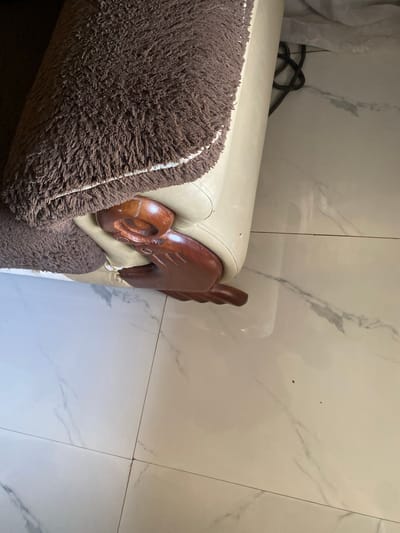 A brown fluffy blanket is draped over the side of a cream-colored sofa. The sofa has a carved wooden leg that is elaborately shaped. The floor is tiled with a white marble-like pattern. The scene is indoors and appears to be a living area. The location is Jauro Yinu, Nigeria.