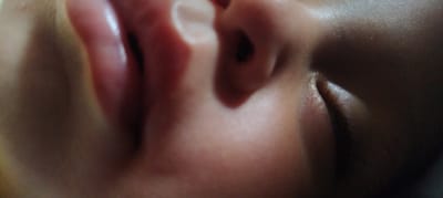 The image shows a close-up of a human face, focusing on the eye, nose, and lips. The eye is closed with dark eyelashes. The nose and lips are pinkish. The image does not provide any location information.