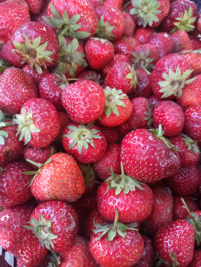 A close-up, overhead shot displays a large pile of fresh, ripe strawberries. The berries are a vibrant red, with visible seeds dotting their surfaces. Many of the strawberries still have their green leafy tops attached. The lighting is bright, suggesting an outdoor setting, possibly a market or a garden. The image does not contain any information about a specific location in Kryvyi Rih, Ukraine.