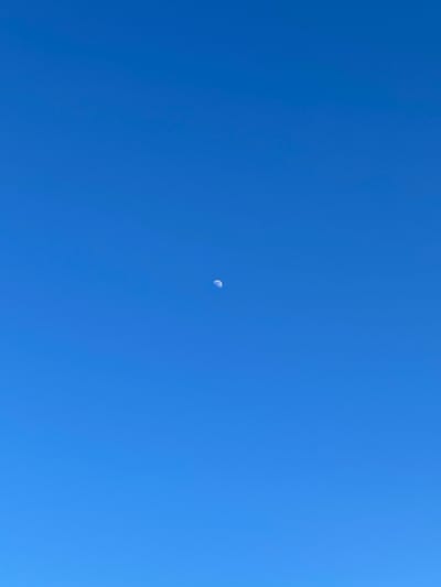 The image shows a clear, bright blue sky. A crescent moon is visible in the center of the frame. There are no other objects or subjects present in the image. The location and city of London, United Kingdom, cannot be determined from the image.