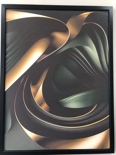 The image shows a framed abstract artwork displayed on a white wall. The artwork features swirling, metallic-like ribbons in shades of dark gray, deep green, and bright gold. The composition is dynamic and flowing, with a sense of depth created by the interplay of light and shadow on the curved surfaces. The frame is simple and black. There is no discernible location in the city of Shymkent, Kazakhstan, or any people, actions, or interactions present in the image.