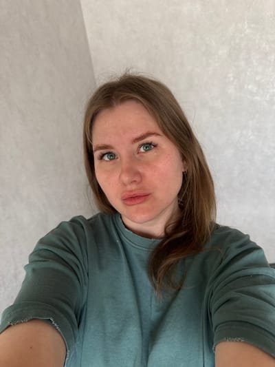 A fair-skinned woman with light brown hair and blue eyes poses for a close-up selfie against a light-colored wall. She is wearing a teal-colored, long-sleeved shirt. The picture is taken at an angle. The location is Gornyi (Dvurechenskoe S/P), Russia. No other objects or interactions are visible.
