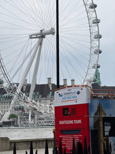 The image shows the London Eye and a Golden Tours bus in London, United Kingdom. The London Eye is a large Ferris wheel with passenger capsules visible. The Golden Tours bus has "Sightseeing Tours" printed on the side, along with phone number 020 7233 7030 and web address www.goldentours.com. The Houses of Parliament and Elizabeth Tower are visible on the side of the bus.