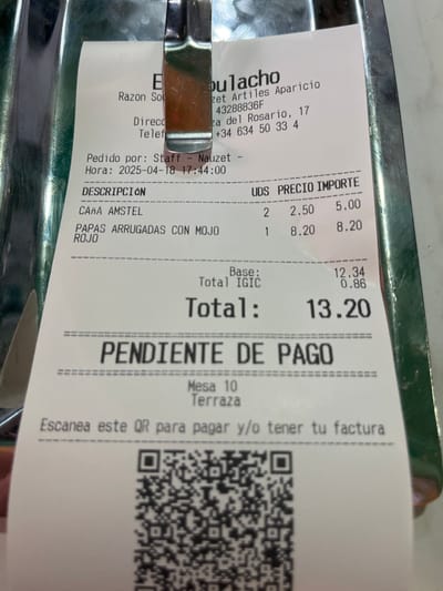 The image is a receipt from a restaurant called "El Goulacho", located in Agüimes, Spain at coordinates 27.907, -15.447. The receipt shows an order for two "Caña Amstel" and one "Papas arrugadas con mojo rojo". The total bill is 13.20 euros and is marked "Pendiente de pago" indicating it's still pending payment. The receipt also includes a QR code for payment and the table number, which is 10, located on the terrace. The receipt was issued on 2025-04-18 at 17:44:00 by a staff member named "Nauzet".  The receipt is partially obscured by a green object in the top right corner.