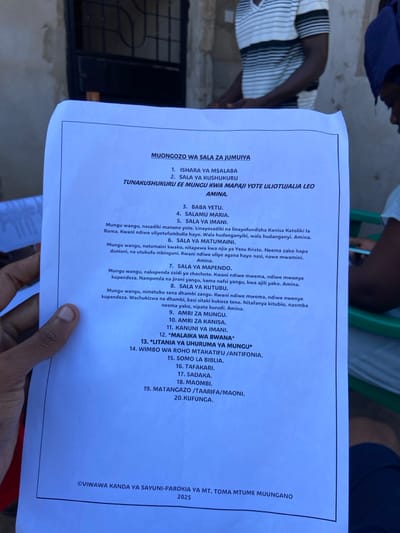 The image shows a piece of paper on a table, displaying a list of 20 Swahili phrases for prayer, titled "Muongozo wa Sala za Jumuiya" (Guide to Community Prayers). The paper is likely from a church or religious institution in Dar es Salaam, Tanzania. The location, based on the provided coordinates, is in the densely populated area of Mbezi Louis, within the Kinondoni district. The environment appears to be a simple indoor setting with a table and people in the background, though they are out of focus. The paper is the primary subject of the image, and the people in the background are not clearly identifiable. The scene is static and devoid of any particular action or interaction. The image appears to be captured with a handheld device, showcasing the paper with a slight tilt.