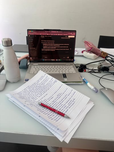 The image shows a desk with a laptop, notebook, pen, and other objects. The laptop is open, displaying a text editing interface and search results about legal entities, with notes on the right. A red pen rests on the notebook, which contains handwritten notes related to legal capacities and entities, including "Incapacities of Adults DE IURE", "Legal Entities", and "Non-Profit Entities". The desk also contains a water bottle, a correction pen, and a computer mouse. The laptop is a Lenovo Yoga model. The environment is an indoor setting, likely a home office, but there is no information that helps determine the location is in the city of Milan, Italy.