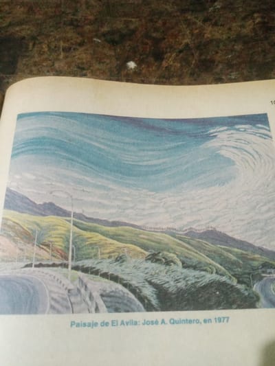 The image is a painting of a landscape titled "Paisaje de El Ávila: José A. Quintero, en 1977." The scene depicts a winding road with streetlights in the foreground, leading towards rolling green hills that recede into distant mountains. The sky is a swirling expanse of blue and white, suggesting clouds or wind. The painting appears to be a reproduction within a book or magazine, as indicated by the visible page border and a small number "10" at the top right. The text below the painting identifies it as a landscape of El Ávila, painted by José A. Quintero in 1977. El Ávila National Park is located in the Venezuelan Coastal Range, near the city of Santa Ana, Venezuela.