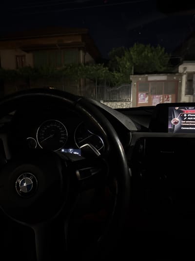 The image, taken at night from inside a car, shows the dashboard and the view through the windshield. The dashboard displays a speedometer reading of approximately 20 km/h and a digital display showing the time as 22:17 and a car with the letter "P" indicating park, with a distance of 143 km. The central infotainment screen shows options for "Not connected," "iPhone," "AUX," "Set wireless connections," and "Connections." Outside the car, a residential building with a brown roof and green-shuttered windows is visible, along with trees and a metal fence. The location is identified as Zverino, Bulgaria.