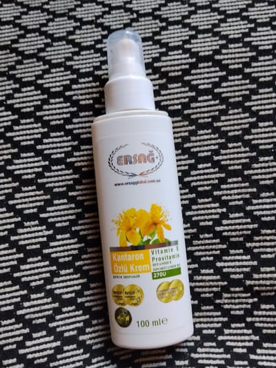 A white plastic bottle with a pump dispenser and a clear cap is placed on a black and white patterned surface. The bottle contains a cosmetic product labeled "Kantarol Özlü Krem" with additional text in Cyrillic script. The label features a logo that reads "ERSAG" and a website address "www.ersagglobal.com.ua". Yellow flowers are depicted on the label. There are also circular seals on the bottle with text indicating "ВИБІР" and years like "2020", "2021", "2014", and "2013". The volume of the product is indicated as "100 mle". The scene appears to be indoors, with the patterned surface possibly being a textile like a rug or a tablecloth. No people are visible in the image. The lighting suggests it could be daytime, but no specific time or weather conditions can be determined. The location context provided is Cîrpești, Moldova.