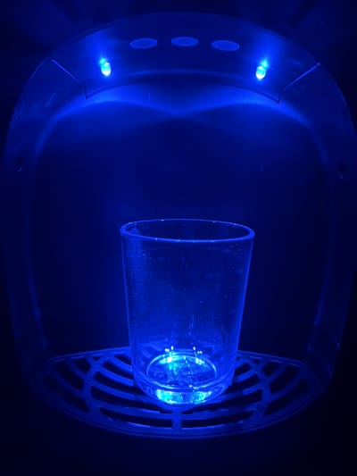 A cylindrical glass object is mounted within a blue illuminated device. The device appears to have a round exterior with ventilation slats on one side and indicator lights on the other. The setting is dark. There is no evidence to suggest that the picture was taken in Even Yehuda, Israel.