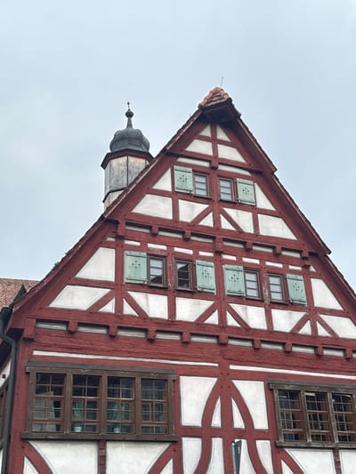 The image shows a close-up of a red and white timber-framed building with a steep, tiled roof. The building has multiple windows with light green shutters. A dark, octagonal tower with a pointed roof is visible behind the main building. The sky is overcast and gray. The building appears to be located in the historic center of Sindelfingen, Germany, possibly on the Marktstraße, given the architectural style which is characteristic of the region. No people are visible in the image.