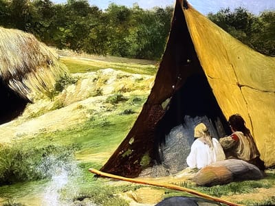 This painting depicts a primitive settlement set in a natural, verdant landscape, located in the city of Reus, Spain. In the foreground right, two individuals are seated or kneeling at the entrance of a large, conical or A-frame tent-like structure, rendered in shades of yellow and tan, with dark internal supports. The individual on the left wears light-colored garments and a head covering, while the person on the right has dark, long hair and is dressed in earth tones with a reddish detail on the upper back. They are positioned with their backs partially to the viewer, facing inwards or slightly to the left, towards a dark interior. A dark, rounded object rests on the ground directly in front of them. In the lower-middle foreground, a long, light-brown wooden staff or pole lies diagonally on the grass. To the left, a rounded, thatched hut-like structure is partially visible, its straw-colored roof prominent against the green surroundings. The landscape features rolling hills covered in lush green and yellow-green vegetation, with dense forestation forming a dark green backdrop across the upper mid-ground. Above the treeline, a light blue sky with faint cloud formations is visible. A bright, light-colored patch on the ground in the lower-left suggests a reflective surface or disturbed soil, possibly near a water source. The scene is illuminated by natural daylight.
