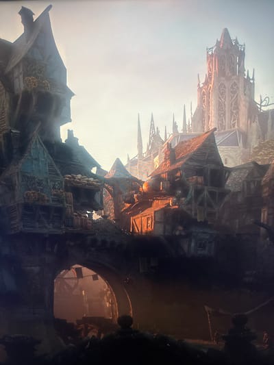 The image depicts a fantasy or medieval-style city scene, with an arched entryway in the foreground leading to a dimly lit interior, possibly a tunnel or courtyard. Above the archway and extending into the background are numerous buildings with steep, pitched roofs, many appearing weathered and constructed with wood and stone. Some structures exhibit a timber-framed design. In the far background, a tall, ornate gothic-style structure, resembling a cathedral or a grand tower, rises against a hazy sky. The overall lighting suggests either dawn or dusk, with warm, golden hues illuminating parts of the city. There are no discernible people or specific identifiable landmarks that would place this scene in Herzliya, Israel. The image appears to be a digital rendering or artwork.