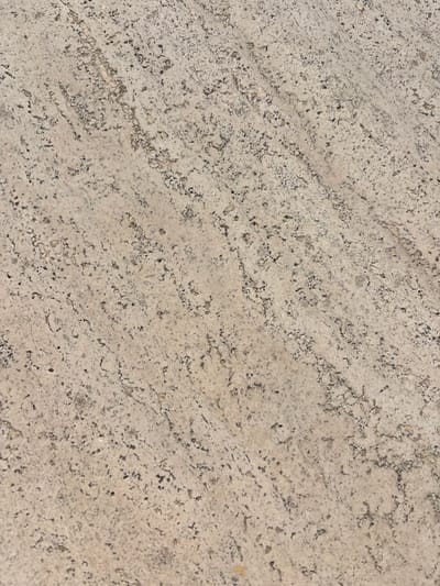 The image shows a close-up of a textured stone surface. The stone is predominantly light beige or off-white with dark grey or black speckles and small grooves. The pattern is linear, running from the top left to the bottom right of the image. It has a rough and porous texture. It may be of travertine stone, which is common in Rome, Italy. However, without additional information, the precise location and origin of the stone cannot be determined.