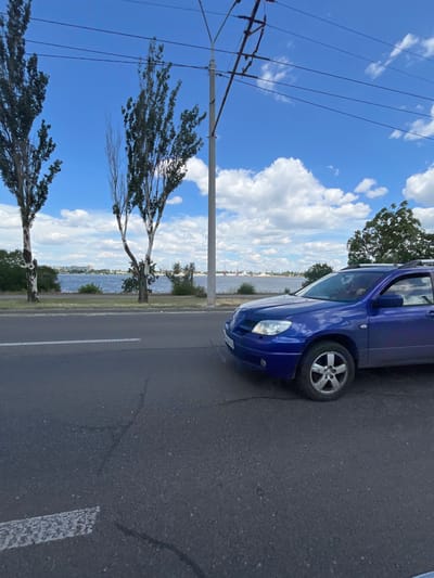 The image shows a blue car parked on the side of a road, with the sea in the background. The sky is blue with white clouds, and there are trees on the left side of the image. The image is taken from a low angle, looking up at the car and the sky.
The car is a hatchback, and it is parked on a paved road. The road has a white line painted on it, indicating a lane. The sea is visible in the background, and there are some buildings on the other side of the sea. The sky is blue with white clouds, and the sun is shining. There are trees on the left side of the image, and they are green and leafy. The image is taken in daylight, and the weather appears to be good.
The image is taken in a coastal area, and it is likely a sunny day. The car is parked on the side of the road, and it is not in use. The sea is calm, and there are some boats in the distance. The trees are green and leafy, and they are providing shade. The sky is blue with white clouds, and the sun is shining. The image is taken in daylight, and the weather appears to be good.
There is no visible text in the image. The image is of a car parked on the side of the road, with the sea in the background. The sky is blue with white clouds, and there are trees on the left side of the image. The image is taken from a low angle, looking up at the car and the sky.
