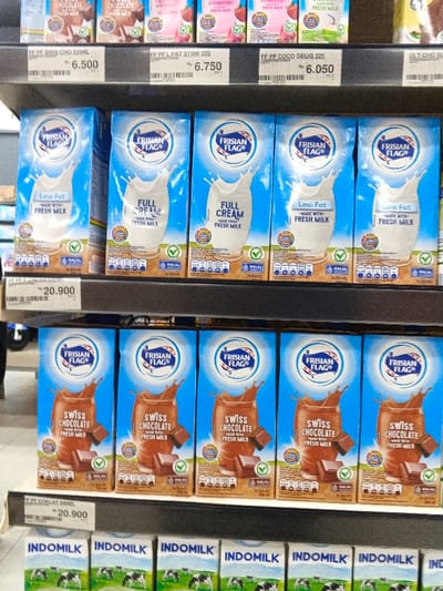This is a shelf display of Frisian Flag milk products. The top shelf features chocolate, strawberry, and coconut flavored milk in small cartons priced between Rp 6.050 and Rp 6.750. The second shelf displays Frisian Flag milk in "Low Fat" and "Full Cream" variants. Below, "Swiss Chocolate" flavored Frisian Flag milk cartons are visible. The bottom row shows "Indomilk" cartons. Prices for the "Swiss Chocolate" and "Low Fat"/"Full Cream" milk cartons are displayed as Rp 20.900. All Frisian Flag products bear a "Halal" certification mark.