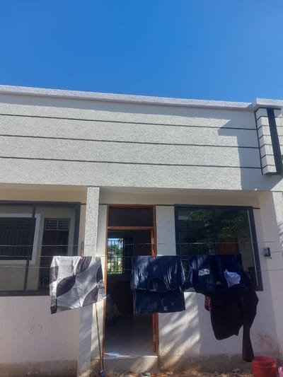 The image depicts a building under a clear blue sky. Clothes are hanging on a clothesline strung between the building's floors. The building has a textured exterior, with dark-framed windows. The location of the building is Dar es-Salaam, Tanzania.
