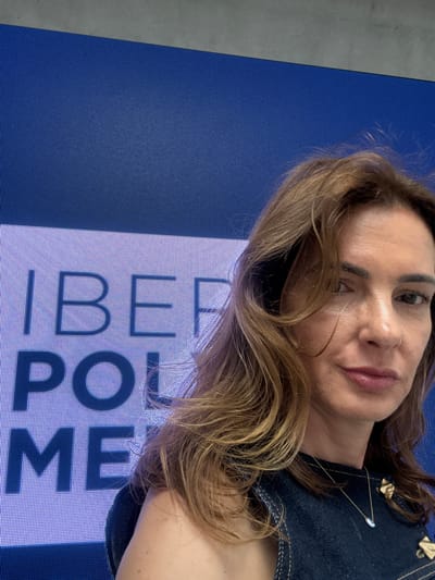 A woman is lying on a blue LED screen display. The display shows the text "IBEF PROME" in large, white capital letters against a blue background. The location is Torres Vedras, Portugal, given the text is associated with the PROME conference that happens there.