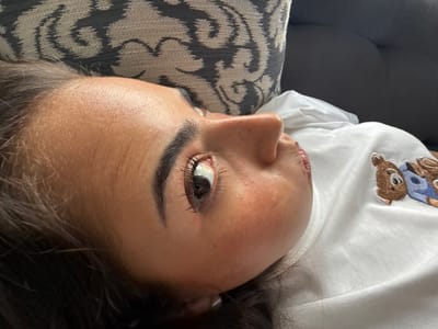A close-up shot focuses on a person lying down. The person is fair-skinned with dark hair. A decorative pillow is behind the person. The person wears a white shirt. The setting is indoors. There is no indication that the scene is in San Bernardino Tlaxcalancingo, Mexico.
