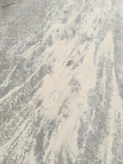The image depicts a concrete surface, likely a floor or pavement, partially covered with a light-colored, powdery substance, possibly sand or dust. The substance is distributed unevenly, creating streaks and patterns across the gray concrete. The location in the city of Uyo, Nigeria is not confirmed.