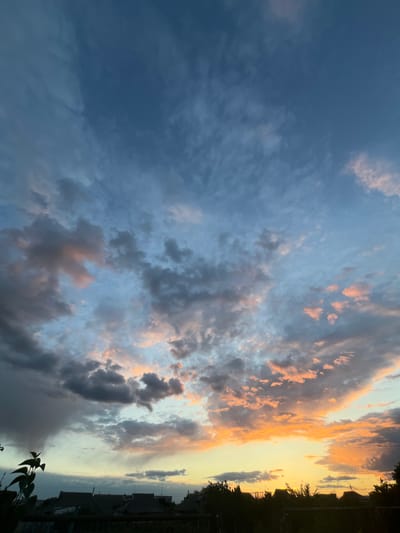 The image shows a sky with a mix of dark gray and light orange clouds. The orange clouds are concentrated near the horizon, suggesting a sunset or sunrise. In the bottom right corner, there is some foliage, indicating the presence of trees or bushes. The image is taken from Slobozia, Moldova. There are residential buildings at the horizon. The buildings are silhouetted against the sky.