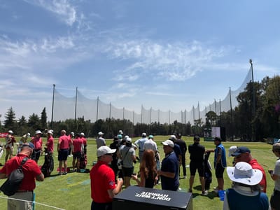 The image shows a gathering of people, predominantly men, on a grassy field with golf equipment. Many are wearing golf attire, including hats and golf shirts. A large net structure stretches across the background of the field, likely a driving range or practice area. There's a digital scoreboard visible in the distance between the net structure and trees. A black cooler with the white text "DON'T WAIT, HYDRATE" is in the foreground. The location is Naucalpan de Juárez, Mexico.