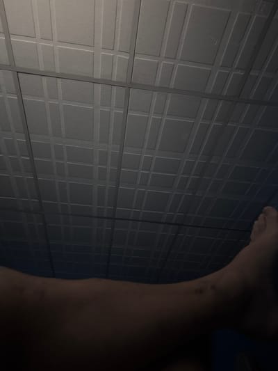 A close-up, low-angle shot shows a section of a wall constructed from square panels, each with a raised square pattern within. The wall is gray or dark in color, and the lighting creates a shadowed effect. In the right portion of the frame, a human arm is partially visible, its skin tone lighter than the wall, casting a shadow and obscuring the view. The photo does not contain enough information to determine the location in El Bajío, Venezuela.