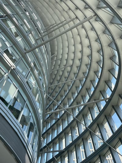 The image captures an interior view of a modern architectural structure, likely in the Chaoyang District of China. The structure features a curving, glass-paneled roof supported by a framework of metal arches and struts. The glass panels provide natural light and offer a view of buildings outside. The scene lacks any observable individuals or signs indicating specific activities. The architectural style suggests a contemporary design, possibly part of a large public space like a mall, atrium, or transportation hub. The environment is well-lit, and the focus is on the geometric shapes and materials of the architecture.