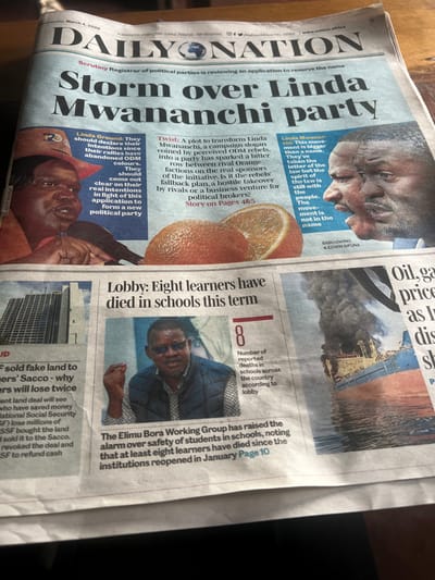 A printed edition of the "DAILY NATION" newspaper, dated Thursday, March 4, 2026, is depicted spread across a surface, likely a wooden table, in Nyeri, Kenya. The newspaper's masthead is prominently visible at the top. The lead headline reads "Storm over Linda Mwananchi party," with supporting articles and images.

To the left of the main headline, an image features a woman identified as Gladys Wanga, with accompanying text discussing the "Linda Ground." To the right, another image displays two men, Babu Owino and Edwin Sifuna, with text related to the "Linda Mwananchi" movement. Between these political articles, two oranges, one whole and one sliced in half, are pictured.

In the lower-center section of the page, a headline states, "Lobby: Eight learners have died in schools this term." This article is accompanied by an image of a man wearing sunglasses and a patterned shirt under a dark vest, gesturing with his right hand. A graphic "8" is positioned next to this image, indicating the number of reported deaths.

Further to the lower-left, a partial article title reads, "Sold fake land to farmers' Sacco - why farmers will lose twice," with a blurred image of a modern high-rise building. In the lower-right quadrant, an article about "Oil, ga price" is visible, featuring a prominent image of a large ship or oil tanker on water, engulfed in thick black smoke from a visible fire. The newspaper is slightly angled from the viewer's perspective, with some portions of the edges subtly out of focus.