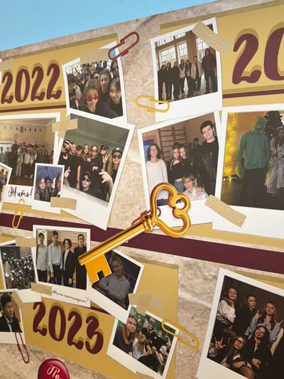 The image shows a collage with the years "2022" and "2023" prominently displayed. It features several photographs of young people, seemingly students, in various group settings. Some photos are attached with tape and paper clips. A large, golden key is centrally positioned over the collage. The collage is set against a pale, marbled-look background, and a portion of blue is visible on the left. There is no information to indicate this is Podolsk, Russia.
