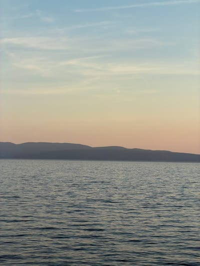 The image shows a landscape view, split vertically into three distinct sections. The left section depicts a blue sky with light clouds. The middle section shows a coastal mountain range. The right section contains water with wave patterns, potentially a lake or sea. The image is oriented vertically, not horizontally. The location is likely near Grad Rijeka, Croatia, given the presence of coastal mountains and a body of water.