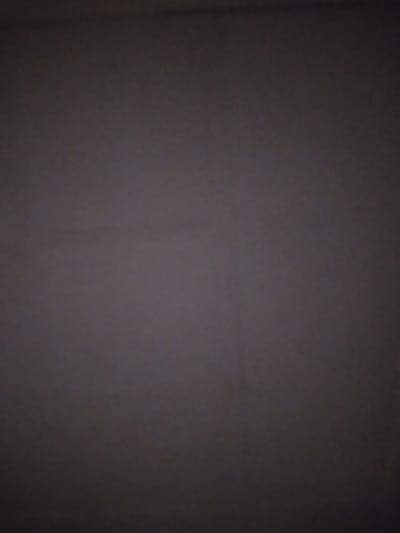 The image depicts a dark, nondescript surface, possibly a wall or a textured fabric. There are faint, vertical lines visible, suggesting a subtle pattern or texture on the surface. The lighting is dim, creating a somber and underexposed atmosphere. No people, objects, or discernible environmental features are present. The image does not provide any information that can be used to identify its location in Ilorin, Nigeria.