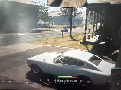 The image depicts a video game scene. In the foreground, a white coupe-style car is parked on a street. The car has a sleek design with two doors and a sloping roofline. In the background, a residential street is visible with houses and trees. There are other vehicles in the distance, and a person can be seen sitting on the porch of a house. The overall setting appears to be a suburban or small-town environment. The image is a screenshot, evidenced by the user interface elements at the bottom, including a speedometer showing speed and other game-related information. The scene does not show any recognizable landmarks or features that would specifically place it in Stepnogorsk city administration, Kazakhstan.
