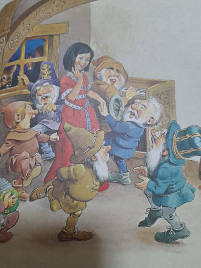 This is an illustration from a storybook, likely depicting a scene from Snow White and the Seven Dwarfs, given the presence of a woman in a red dress and several dwarfs.
The central subject is a woman, presumed to be Snow White, lying on a red surface. She has black hair and is wearing a red dress with blue polka dots and white trim. Around her, several dwarfs are gathered. One dwarf, in a blue jacket and a tall, ornate hat, appears to be bending over her, possibly examining her or offering help. Another dwarf, in a brown tunic and hat, is also close by, his expression unclear. A third dwarf, in a purple cap and tunic, seems to be looking out from behind a wooden structure. Other dwarfs are visible in various poses of concern or interaction.
The setting appears to be indoors, possibly a dwelling or a room within a mine, suggested by the wooden furniture and the general rustic atmosphere. There is a wooden chest or cabinet in the background. The artwork has a whimsical and somewhat exaggerated style, typical of children's fairy tales.
The activity taking place is likely the "awakening" of Snow White, as she appears to be lying down while the dwarfs are attending to her. The dwarfs' expressions range from concerned to perhaps relieved or surprised.
Notable details include the distinct clothing of each dwarf, their expressive faces, and the detailed rendering of the wooden furniture. The overall mood is one of dramatic attention and care for the central figure.
There is no visible text in the image. The location context of Baan Mae Nam, Thailand, does not appear to be directly represented in the visual elements of the illustration.
