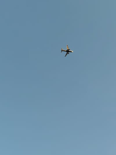 An airplane is seen flying in a clear blue sky. The airplane is a commercial jet with two engines mounted under its wings. It is angled slightly upwards and to the left, appearing to be ascending. The sun is casting a warm glow on the underside of the aircraft, suggesting it is either early morning or late afternoon. The sky is a uniform, soft blue, indicating fair weather with no clouds visible. The scene is devoid of any other objects or elements, focusing solely on the aircraft against the vast expanse of the sky. The perspective is from below the plane, looking up. There is no visible text in the image. The image captures a moment of flight, evoking a sense of travel or transition.