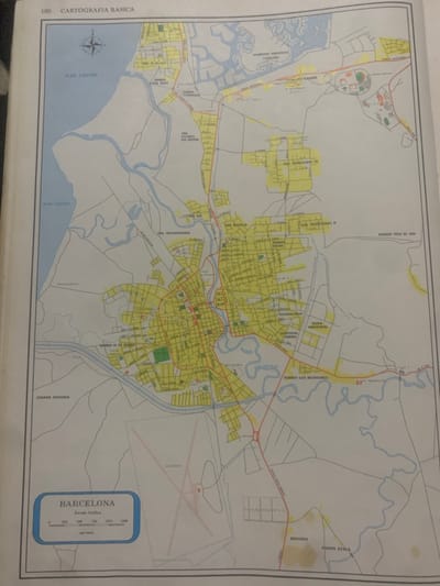 The image is a map of Barcelona, Venezuela, titled "CARTOGRAFIA BASICA". It displays a grid of streets and various named areas such as "MAR CARIBE", "PUERTO NEVERI", "URB. TRICENTENARIA", "ZONA INDUSTRIAL", "MESONES", and "FUENTE AYALA". The map includes a scale in meters and shows bodies of water, roads, and some buildings represented by outlines. The city is situated on the coast, bordering the Caribbean Sea, with a river running through it. An airport, labeled "AEROPUERTO", is visible in the lower right section of the map. There are no people, subjects, or actions depicted in this map; it is purely a geographical representation. The context provided about "La Tagua, Venezuela" is not directly visible or inferable from the map itself.