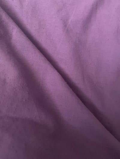 The image shows a close-up, abstract view of a crumpled purple fabric. There are no discernible landmarks or contextual elements to identify a specific location in Kharkiv, Ukraine. The fabric appears to be a textile, possibly clothing or bedding, with slight imperfections or pilling visible in certain areas. The lighting is soft, creating subtle shadows that highlight the folds and textures of the material. The image is solely focused on the fabric itself, with no people, objects, or actions present.