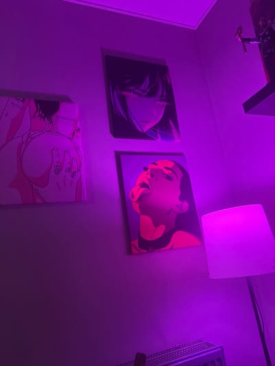 The image presents a room interior illuminated by purple lighting. Three artworks adorn a wall. From left to right and top to bottom:

1.  A square canvas depicting a face obscured by hair.

2.  A square canvas displaying a stylized face, with an open mouth and protruding tongue.

3.  A square canvas showing a person lying down, with their rear towards the viewer and a hand placed on their buttock.

A square white light fixture is mounted on the upper part of the wall. A dark-colored object, possibly furniture, is located at the very top of the image, upside down. A white, grated object is visible on the right. There is no indication of the location being Kudrovo, Russia. No people are visible, only artwork depicting people.