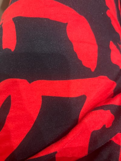 The image shows a close-up of a black fabric with a bold red abstract pattern. The fabric appears to be textured, possibly cotton or a blend, and is creased in several areas, indicating it is likely clothing or upholstery. There are no people, vehicles, or any identifiable elements of the environment visible. The location in Sinyavino, Russia is not discernible from the image content.