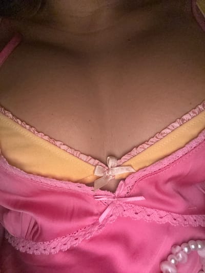 The image is a close-up shot of a person's chest wearing a pink garment layered over a yellow undergarment. Both garments have decorative trim. The pink garment has lace trim and a small pink bow. The yellow garment also has a pink ruffled trim and a small cream-colored bow. The background is out of focus and appears to be the person's skin. There are no discernible environmental elements or indications of a specific location within Palma, Spain.