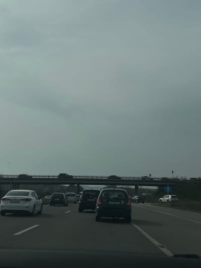 The image depicts a traffic jam on a highway in Lesichovo, Bulgaria. Several cars are closely lined up in the right lane. A bridge is visible above the traffic with cars driving on it. The sky is overcast. The car closest to the viewer has a license plate number of E6832HP. The next car has a license plate number of CA7055BT.