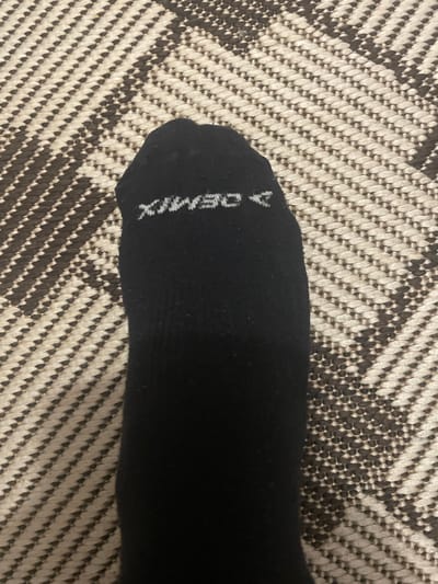 The image shows a black sock with the word "DEMIX" written on it in white. The sock is lying on a rug or carpet with a black and white chevron pattern. The photograph was not necessarily taken in Sarapul, Russia.