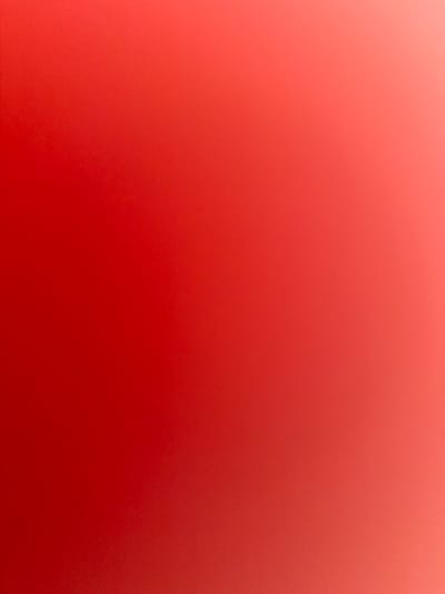 The media file displays an abstract color gradient, smoothly transitioning from a lighter reddish-orange hue in the top-left corner to a deeper, more saturated red in the bottom-right. The gradient presents warm and vibrant tones, ranging from a coral-like shade to a rich, deep crimson. A subtle, uniform grainy or noisy texture is present across the entire image, giving it a consistent visual depth. There are no discernible subjects, such as people or objects, nor is there any specific scene or activity taking place. The image lacks any visual cues that would indicate a time of day, weather conditions, or a specific physical location. No text is visible. While the location context provided is Lusail, Qatar, the image itself does not contain any visual elements or details that relate to or depict this specific geographical location.