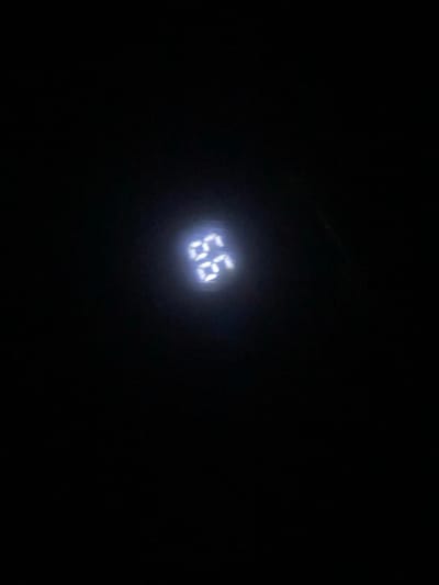 A dimly lit, dark image features a digital display showing the number "66" in bright, white light. The display is the focal point, appearing almost suspended in the surrounding blackness. The overall composition creates a sense of isolation and emphasizes the luminous numerals.