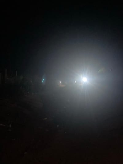 A starkly lit, narrow path recedes into a black, hazy background. A bright light source at the top center dominates the scene, obscuring details with its intense glow. Hints of vegetation and a wall are visible on the right side of the path. The steps lead away from the viewer into the darkness, punctuated by the bright light above and a fainter light source further away. The overall impression is one of stark contrast and obscured visibility.