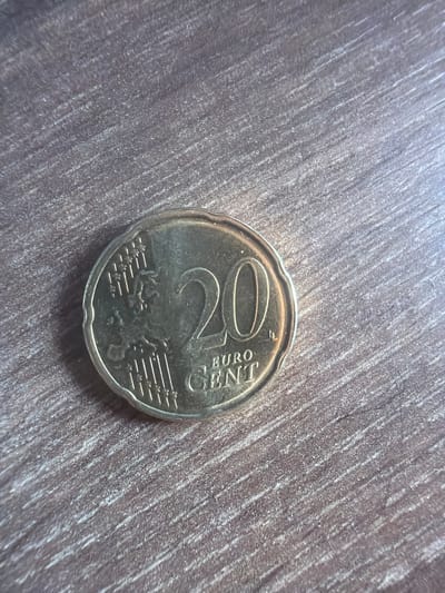 A 20 Euro cent coin lies on a wooden surface. The coin is golden in color and displays the number "20" prominently. The wooden surface has a textured, striated pattern. The image does not provide any information about the city of Kostinbrod, Bulgaria, nor does it depict any people, actions, or interactions.