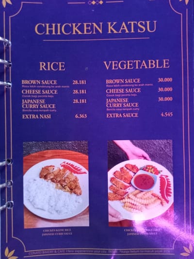 This is a medium shot of a dark blue menu page for "CHICKEN KATSU" dishes at "CONATO BAKERY & CAFE". The menu is organized into two main categories: "RICE" and "VEGETABLE". Both categories offer "BROWN SAUCE" (described as tending towards a sweet taste), "CHEESE SAUCE" (suitable for cheese lovers), and "JAPANESE CURRY SAUCE" (described as having a curry spice flavor).

Under the "RICE" category, the three main sauce options are priced at 28.181 each, with "EXTRA NASI" (extra rice) costing 6.363. Under the "VEGETABLE" category, the three main sauce options are priced at 30.000 each, with "EXTRA SAUCE" costing 4.545.

Two photographs of food items are displayed at the bottom of the page. The left image shows chicken katsu served with white rice, labeled "CHICKEN KATSU RICE JAPANESE CURRY SAUCE". The right image shows chicken katsu served with french fries and a small dish of sauce, held by hands, and is partially labeled "CHICKEN [KATSU] VEGETABLE JAPANESE CURRY SAUCE".

A note at the bottom indicates that "harga belum termasuk pajak 10%" (prices do not include 10% tax). The menu page is held within a spiral binder, visible on the left edge. The image quality is somewhat blurry and features some glare. The setting appears to be an indoor commercial establishment like a restaurant or cafe, consistent with the location context of Situbondo, Indonesia.