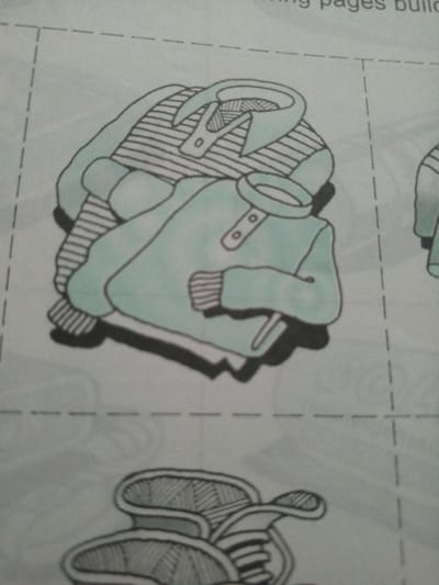 This media file is a drawing of clothing items, possibly intended as a cut-out activity. The main subject is a stack of two garments, rendered in black ink with some areas highlighted in a light teal color. The top garment appears to be a striped shirt or sweater with a collar and buttons. Beneath it is a lighter colored garment, possibly a tunic or kurta, also with a collar and buttons, and striped cuffs. The clothing is depicted as neatly folded.
Below the folded clothing, another object is partially visible, which resembles a pair of shoes or sandals, also drawn with intricate line work and outlines. The drawing is set against a light-colored background with dashed lines indicating perforations, suggesting it is part of a larger sheet designed to be cut out. There is some faint text visible at the top of the image, partially obscured, which appears to read "g pages build".
The drawing style is simple and illustrative. There are no visible people or indications of a specific time of day, weather, or strong emotions. The location context provided, "La Tagua, Venezuela", does not appear to be directly represented within the image itself, suggesting it is external information about the origin or purpose of the media file.